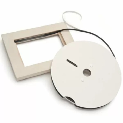 White circular retractable cord reel with a black cord and a square beige mounting frame nearby