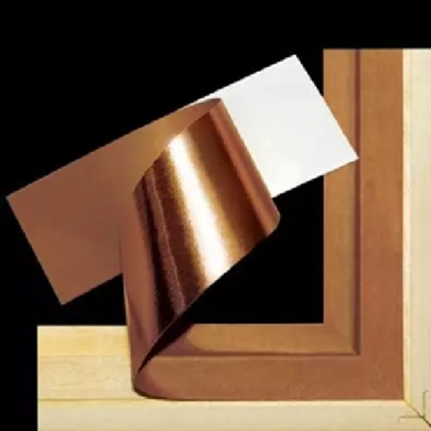 Copper leaf being applied to a wooden picture frame against a black background.